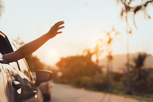 Kvinna som reser med bil en varm solig dag och håller ut handen genom fönstret
